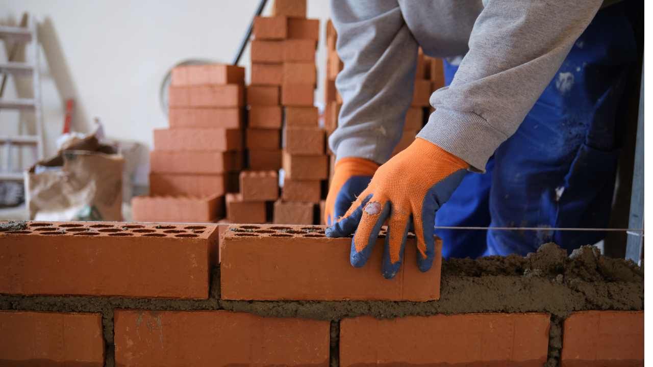 “Worker placing red masonry blocks into fresh mortar during block and retaining wall services in Yorba Linda, CA”