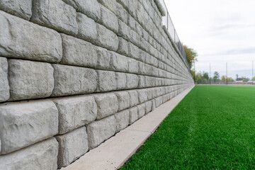 Gray stone retaining wall next to a green turf field.