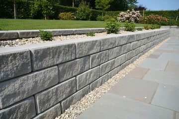 Gray block retaining wall with plants and a stone patio.