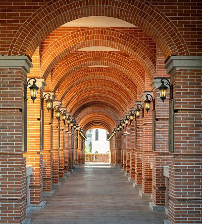A long, symmetrical brick archway lined with glowing wall lamps, leading to an open outdoor space.