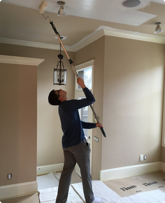 A man is painting a ceiling with a roller