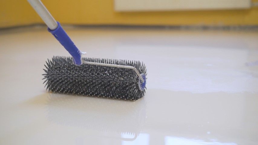 A person is painting a floor with a roller.