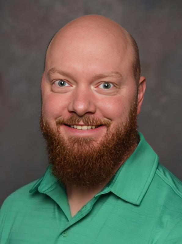 A bald man with a beard is wearing a green shirt and smiling for the camera.