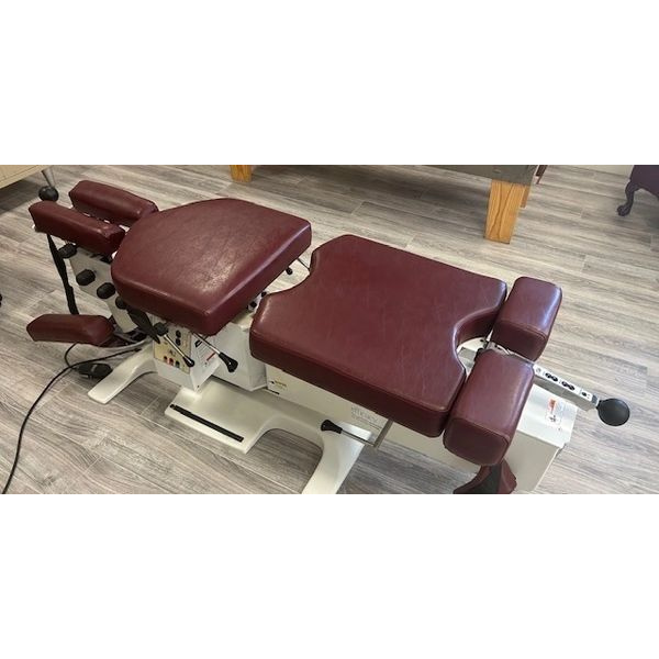 A massage table with a red cushion is sitting on a wooden floor.