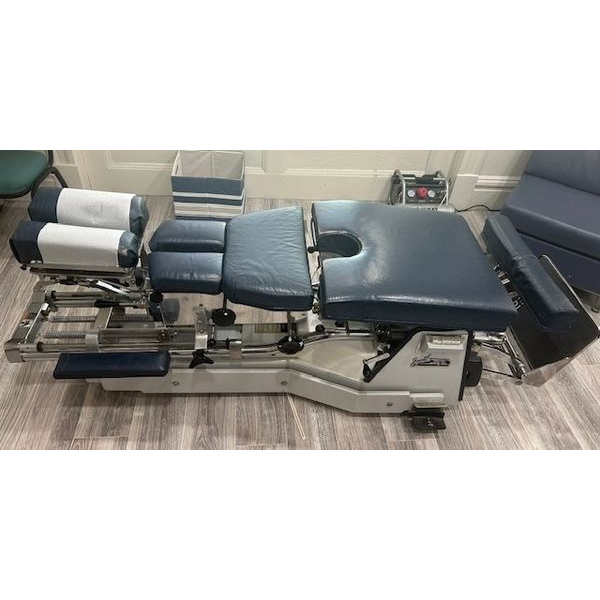 A blue and white chiropractic table is sitting on a wooden floor in a room.