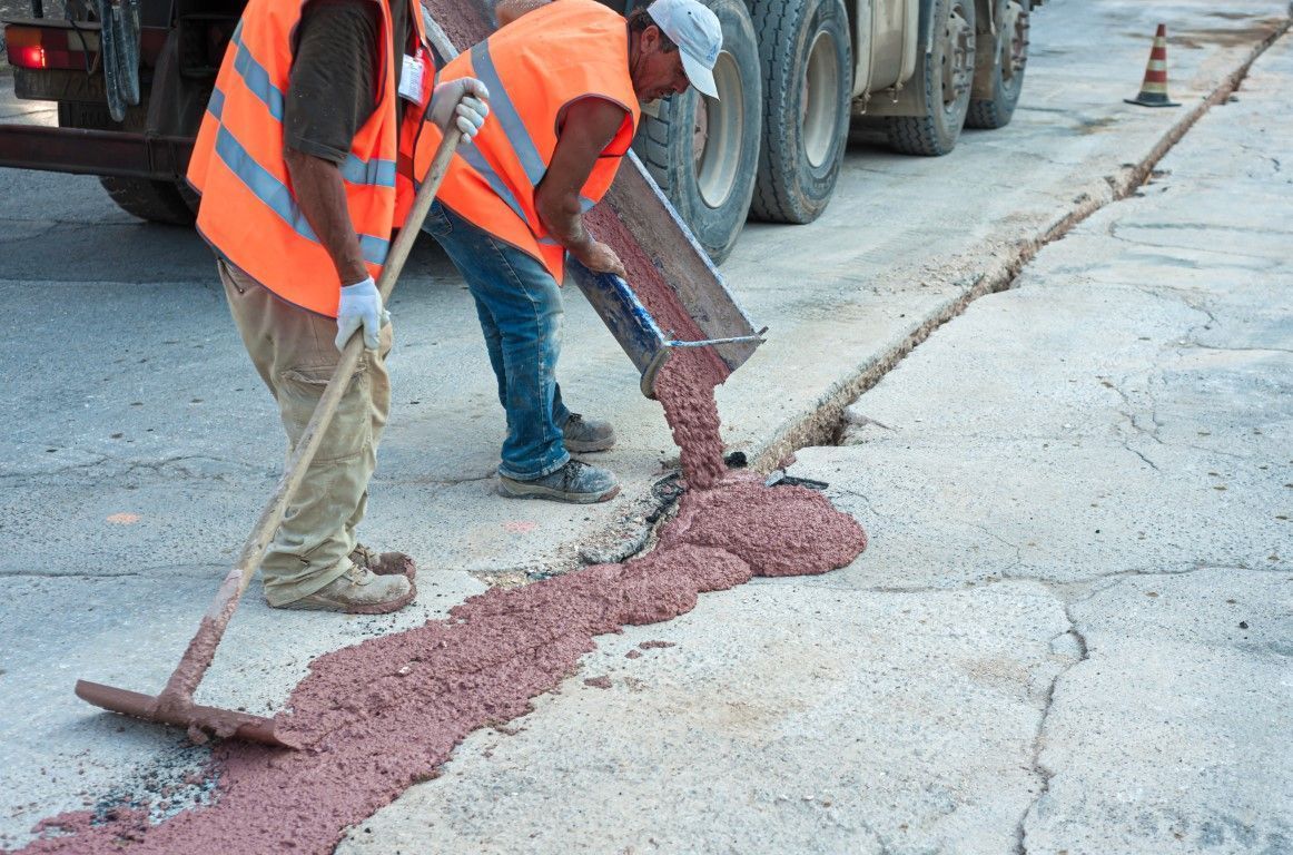Two workers filling a trench with fresh concrete on a sidewalk.