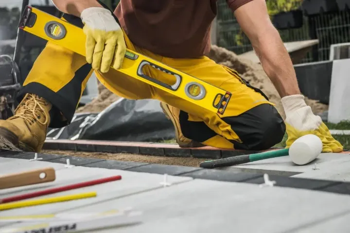 A worker in yellow pants using a level tool on a concrete surface.