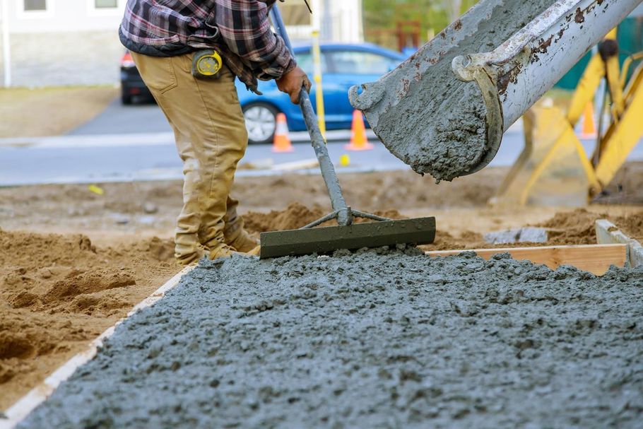 Worker spreading fresh concrete with a rake near a wooden form.