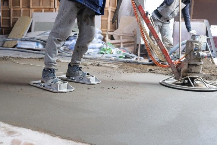 A worker operating a motorized power trowel on a large floor slab.