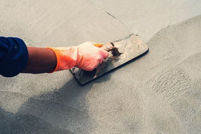 Close-up of a hand in an orange glove using a finishing trowel.