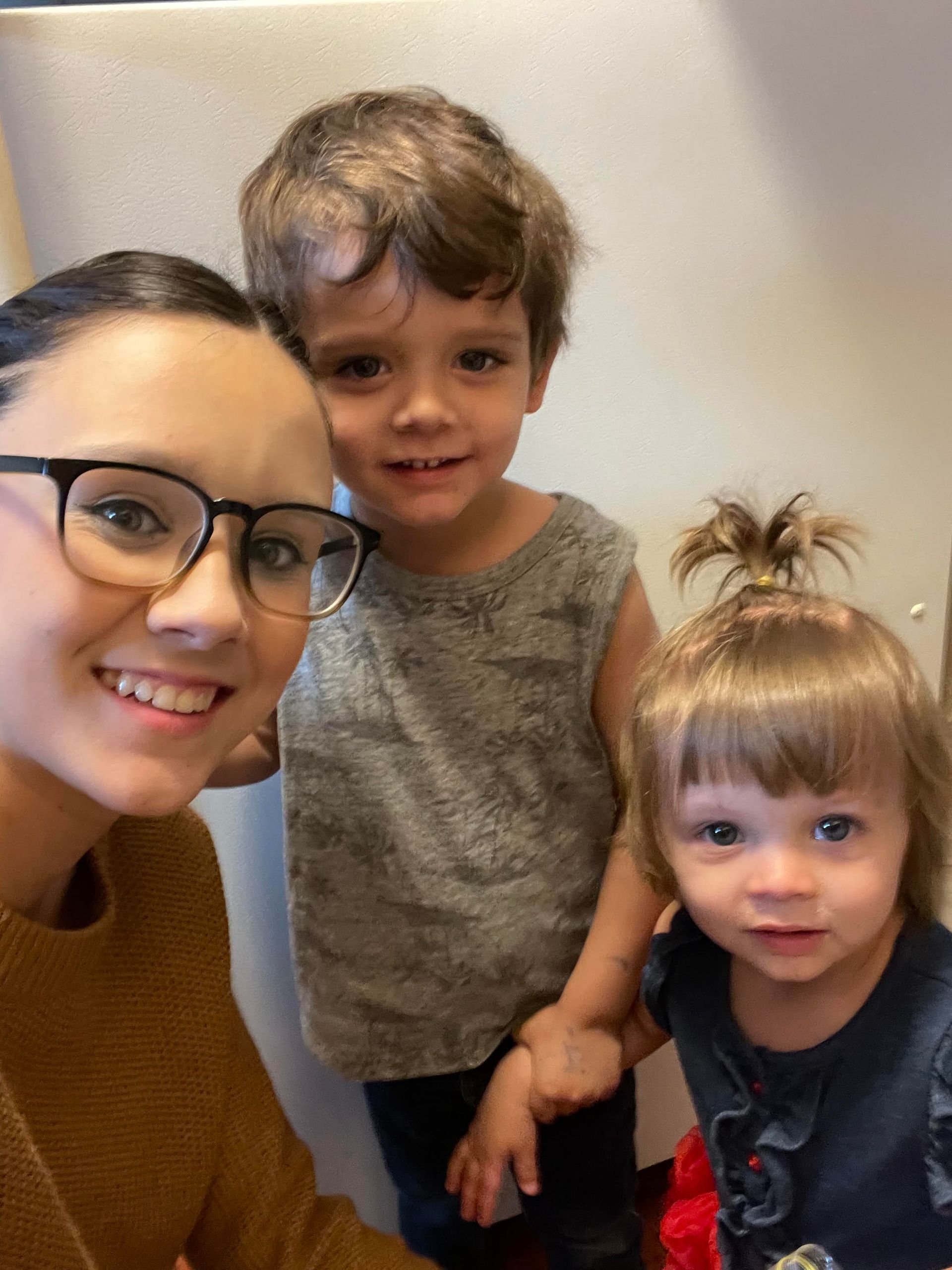 A woman wearing glasses is taking a selfie with two children.