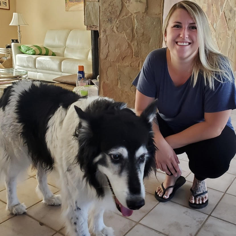 A woman kneeling next to a black and white dog