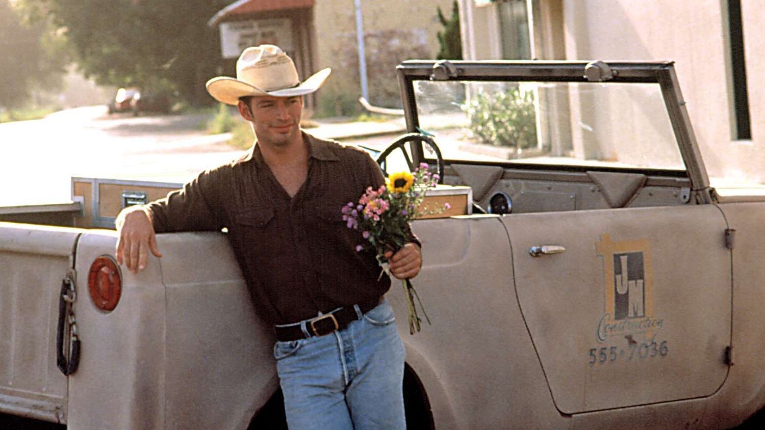 Man in cowboy hat with flowers, leaning on vintage truck in Smithville.