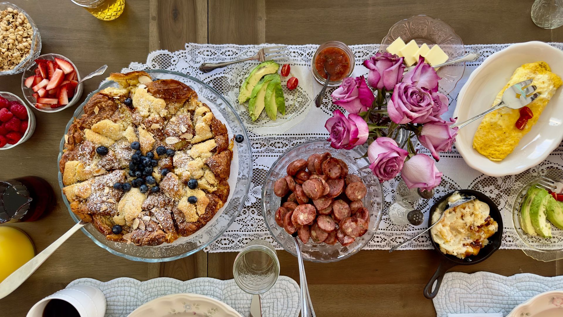 A table topped with platers of breakfast foods and pink flowers.