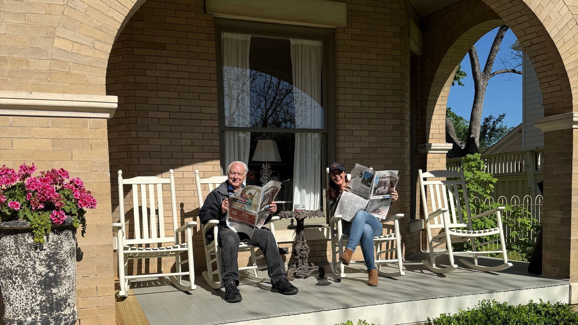 Founder & current Katy House owner reading newspapers on a porch sitting in rocking chairs.