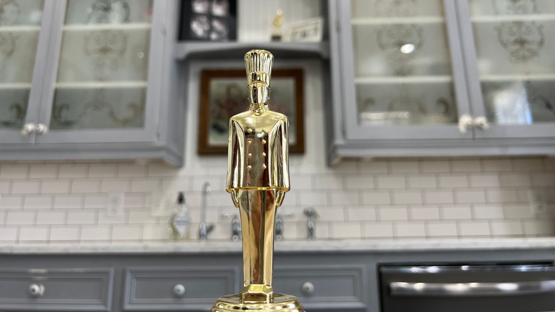 Gold statue of a man standing in front of a kitchen with cabinets.