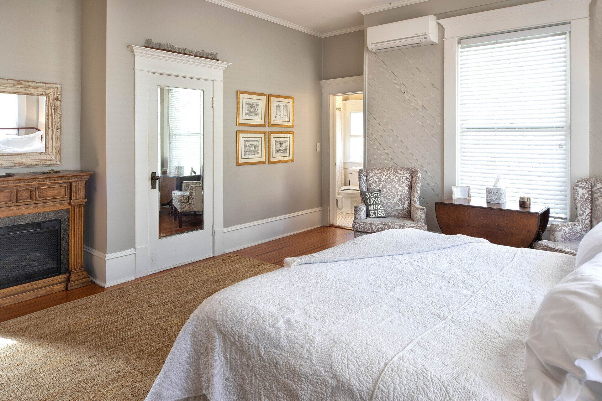 A bedroom with a bed , chair , fireplace and mirror.