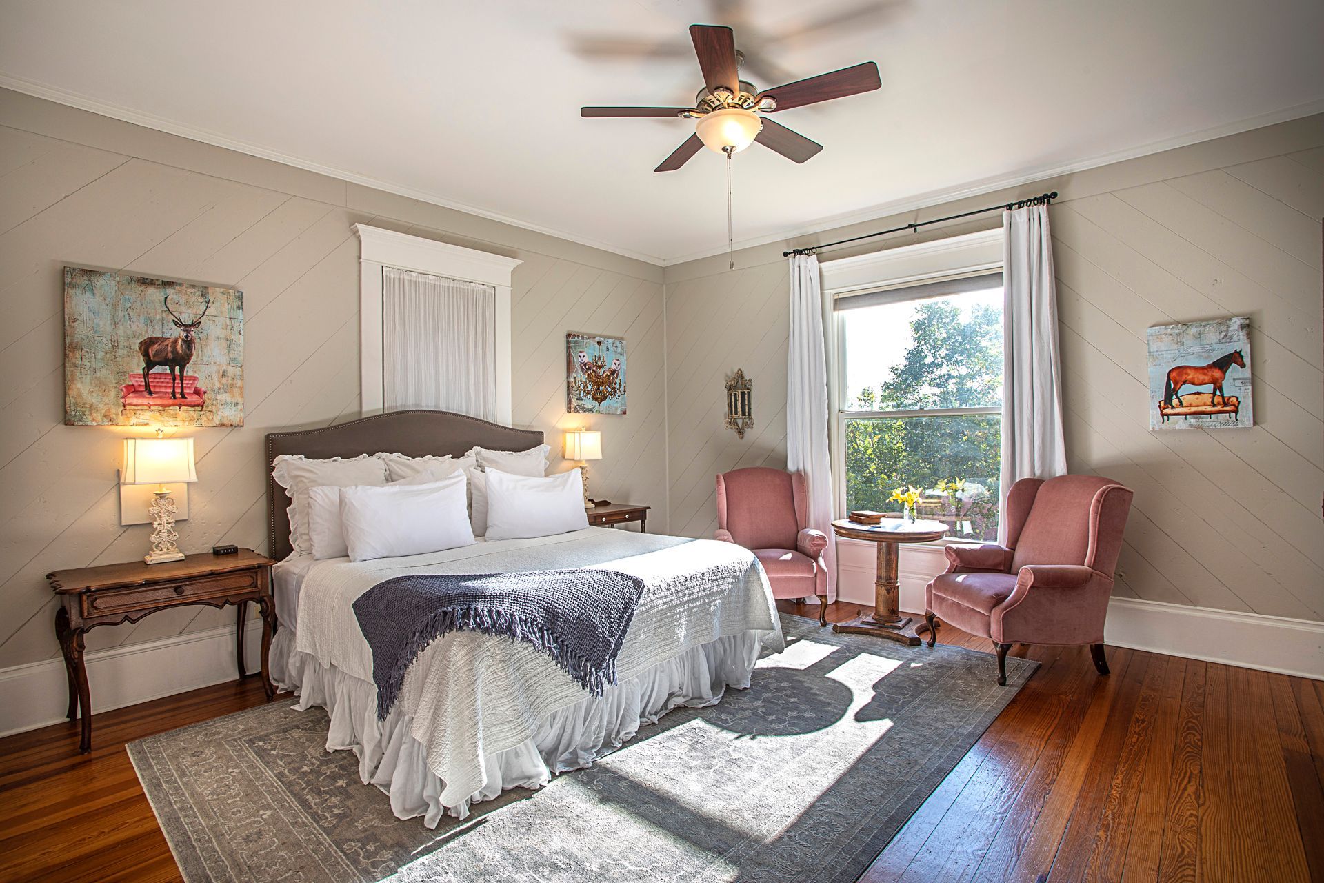 A bedroom with a king size bed , two chairs, a table and a ceiling fan.