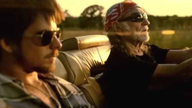 Willie Nelson with son driving in car with the top down on Smithville roads. 