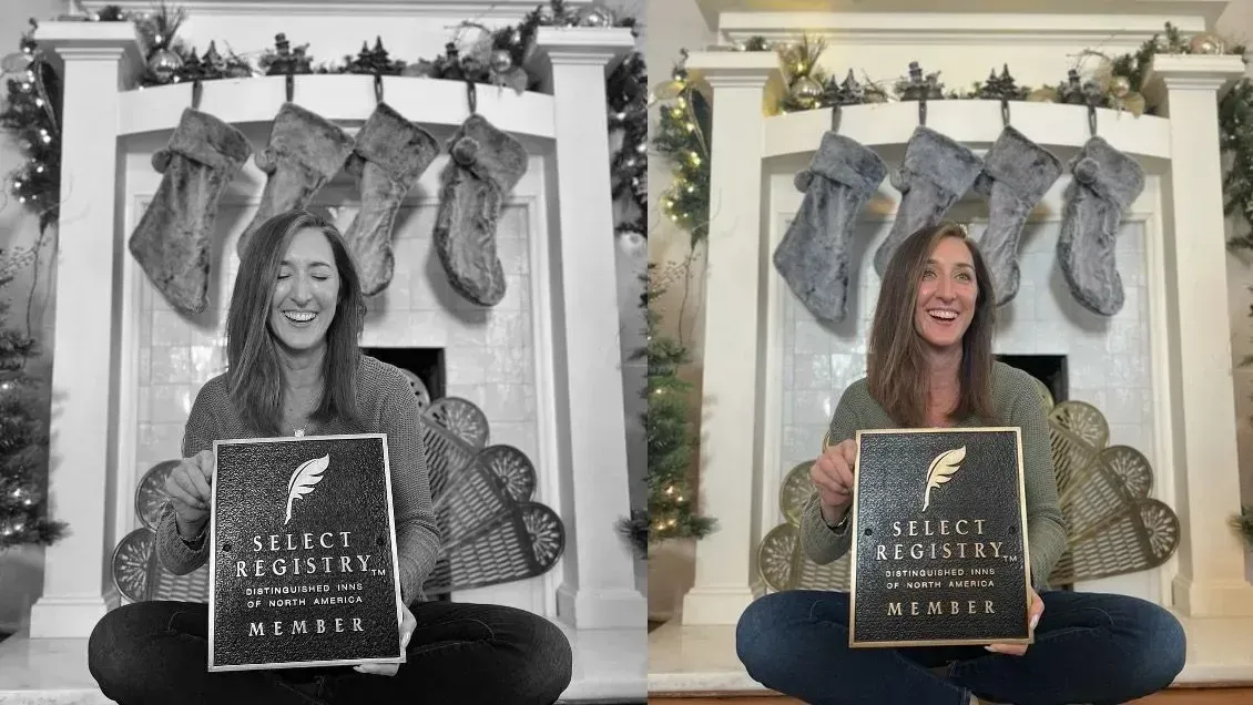 Woman seated, holding a sign in front of a decorated fireplace. Smiling. Wearing a green shirt and jeans.