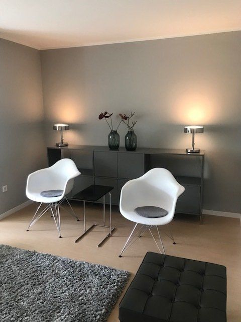 Ein Wohnzimmer mit zwei weißen Stühlen und einem schwarzen Ottomanen