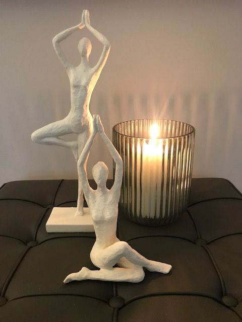 Zwei weiße Frauenstatuen sitzen auf einem Tisch neben einer Kerze