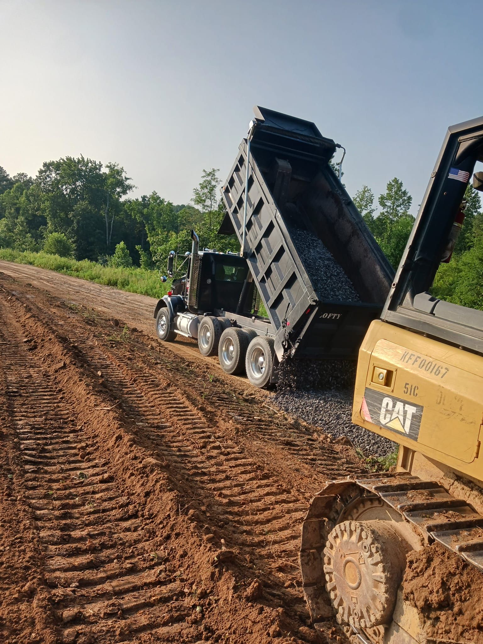 a dump truck is being towed by a bulldozer on a dirt road .