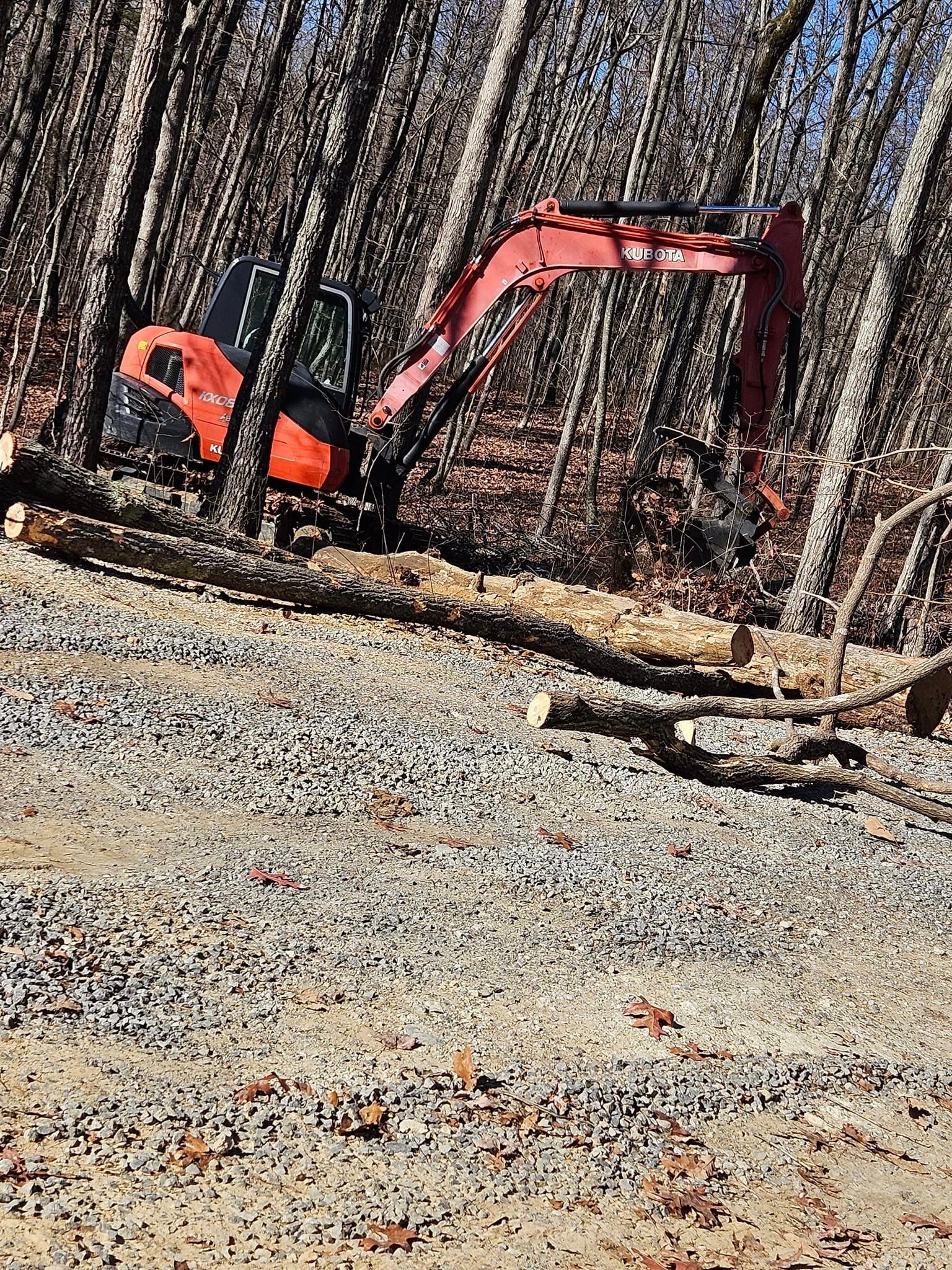 a red and orange excavator is sitting on top of a gravel road in the woods .