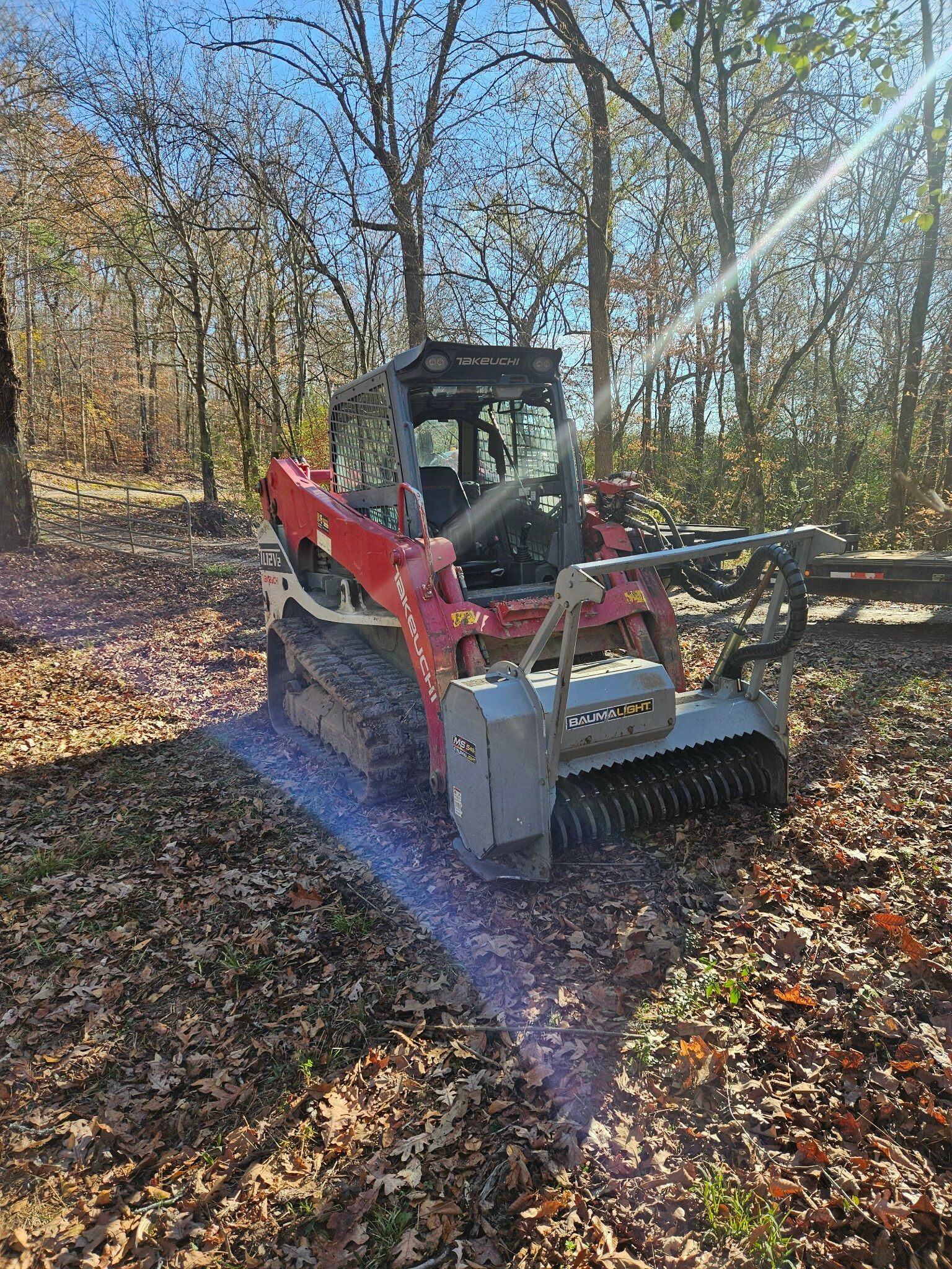 A red and white bulldozer is sitting on top of a pile of leaves in the woods.
