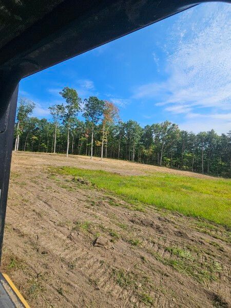 A view of a field from inside a vehicle with trees in the background.