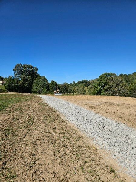A dirt road going through a field with trees in the background.