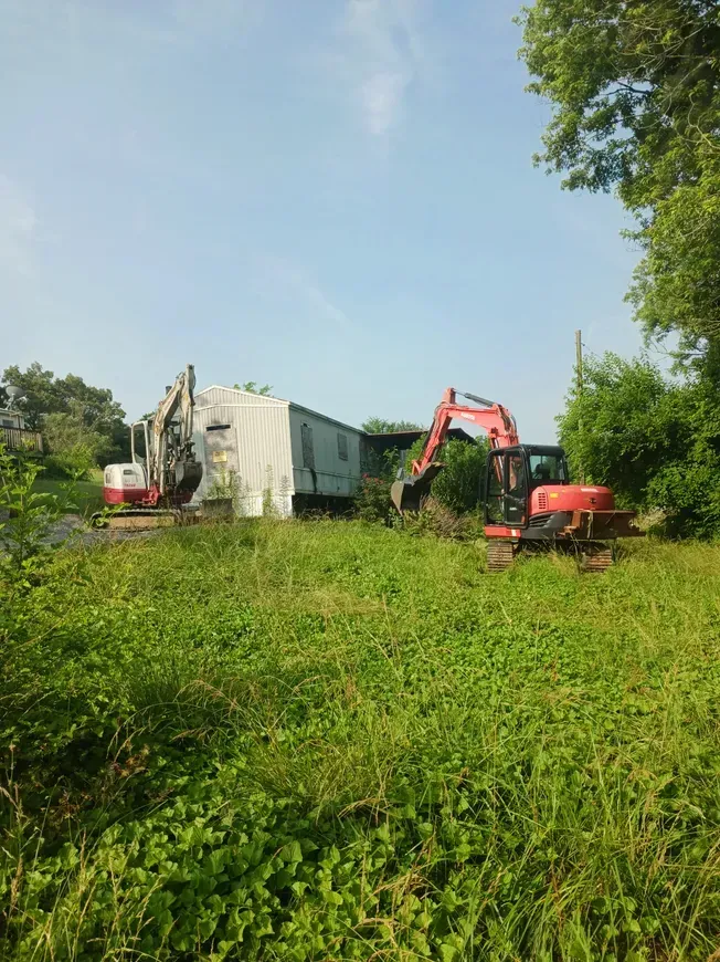 a red excavator is sitting in a grassy field in front of a building .