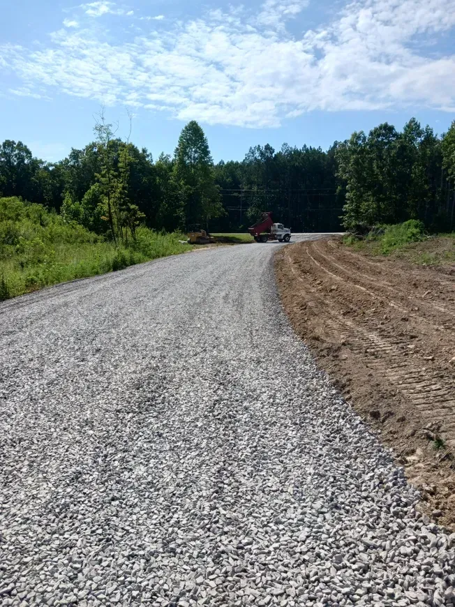 a gravel road going through a field with trees on the side .