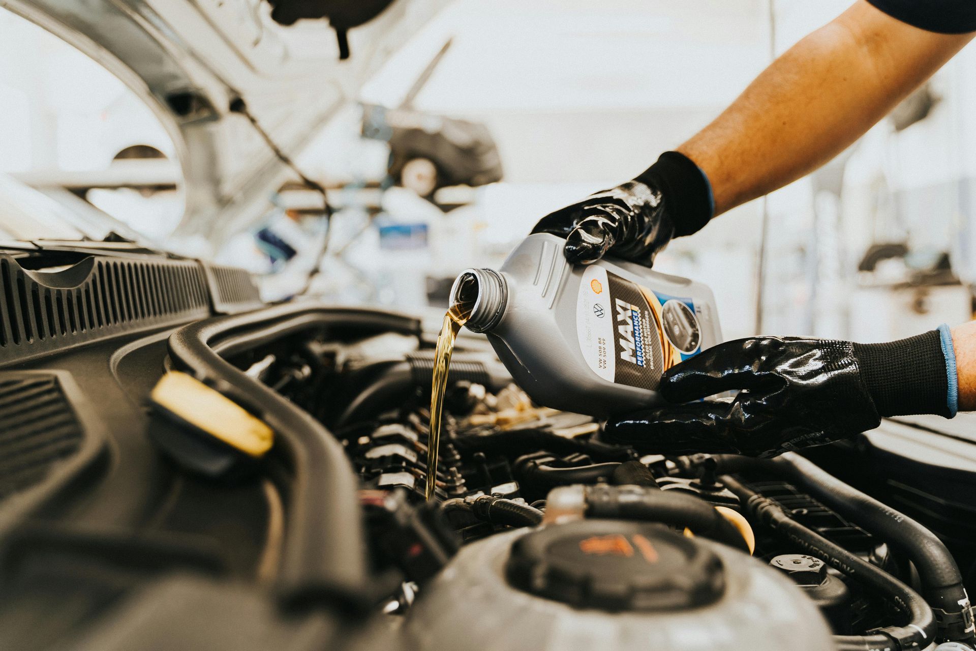 A mechanic pouring motor oil into a car engine; wearing gloves.