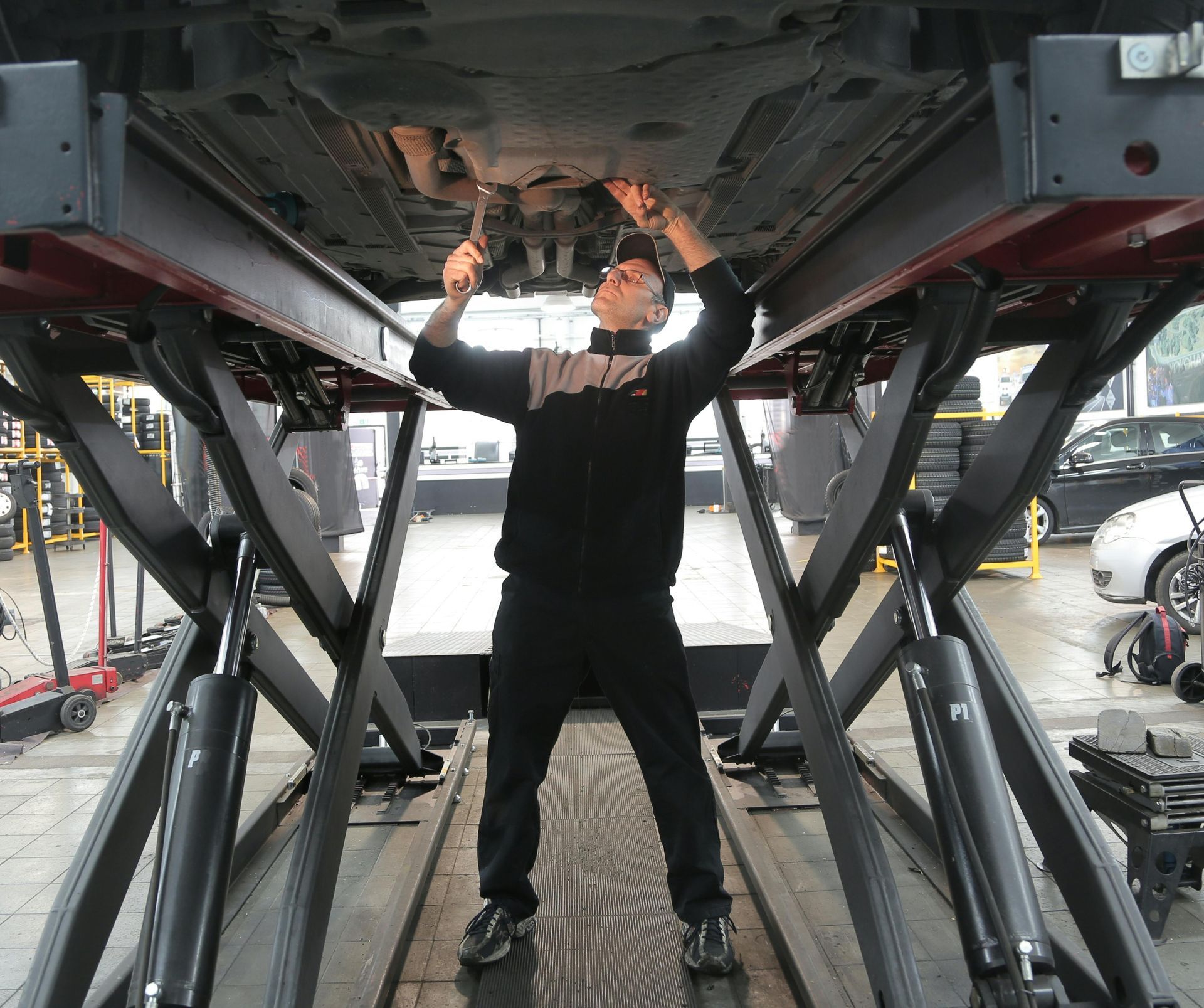 Mechanic working under a car on a lift in a garage.