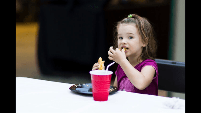 A little girl is sitting at a table eating french fries and drinking a soda.