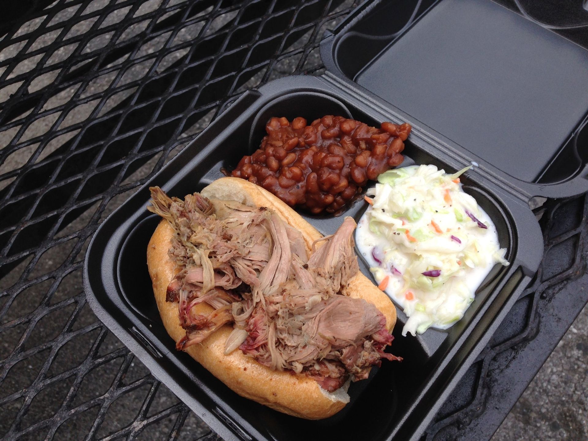 A pulled pork sandwich with beans and coleslaw in a plastic container