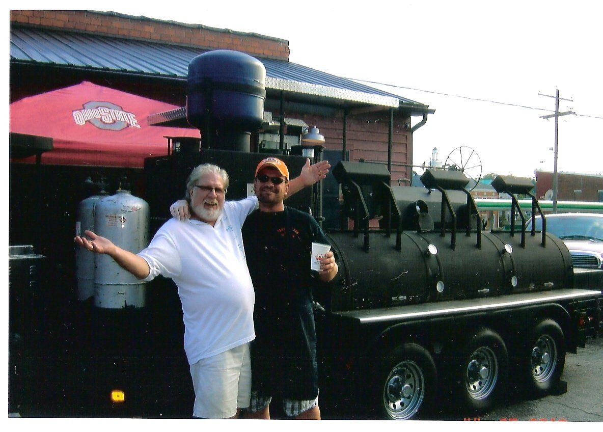 Two men are posing for a picture in front of a bbq truck