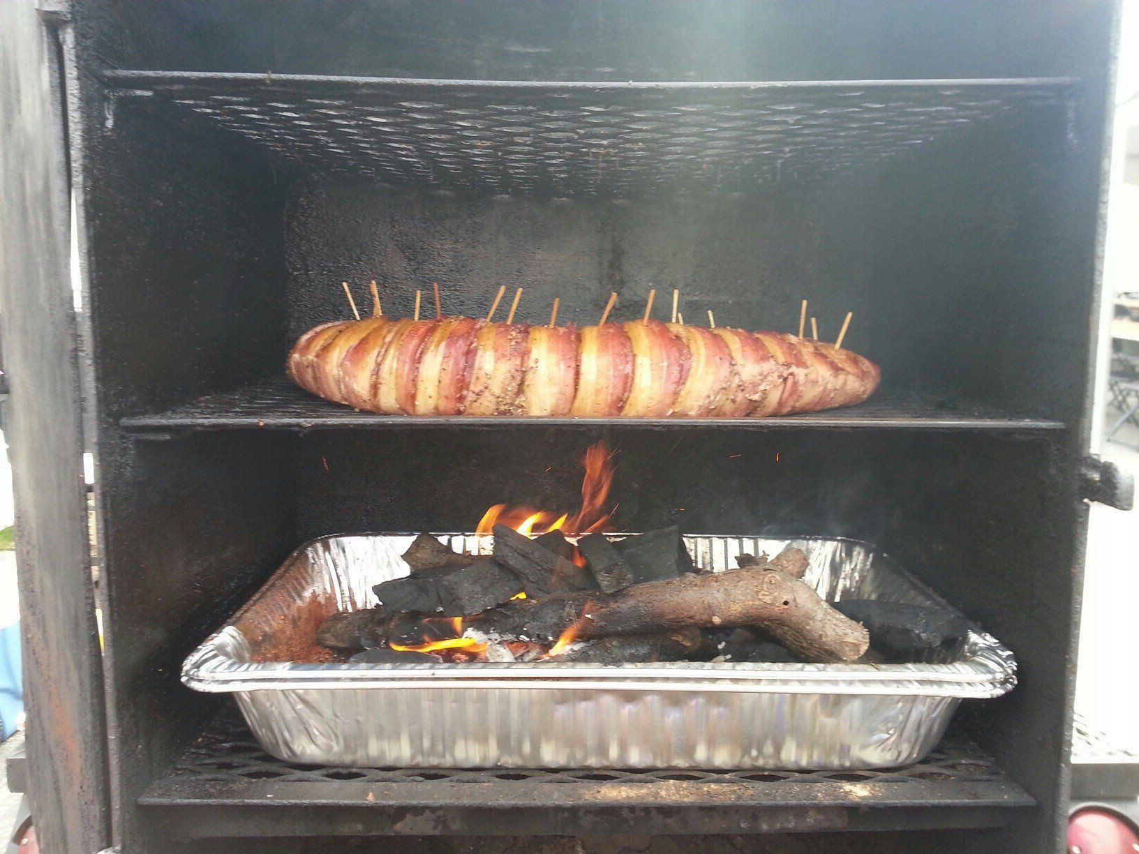 A bacon wrapped sausage is being cooked on a grill.