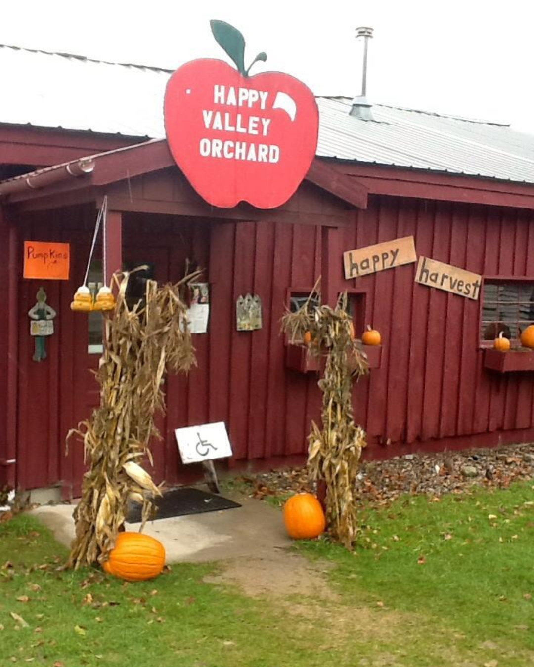 Red building entrance for Happy Valley Orchard, decorated with pumpkins, cornstalks, and