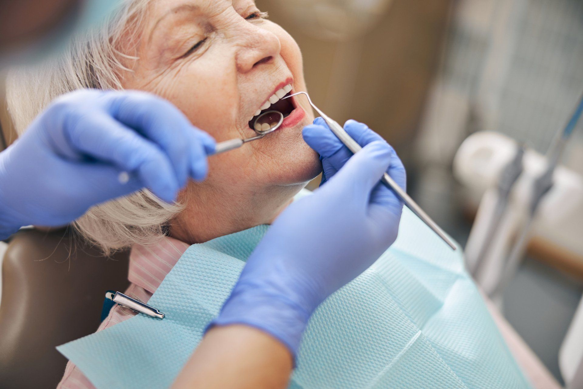 An elderly woman is having her teeth examined by a dentist.