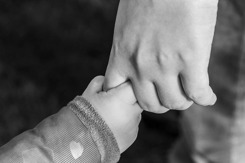 A black and white photo of a person holding a child 's hand.