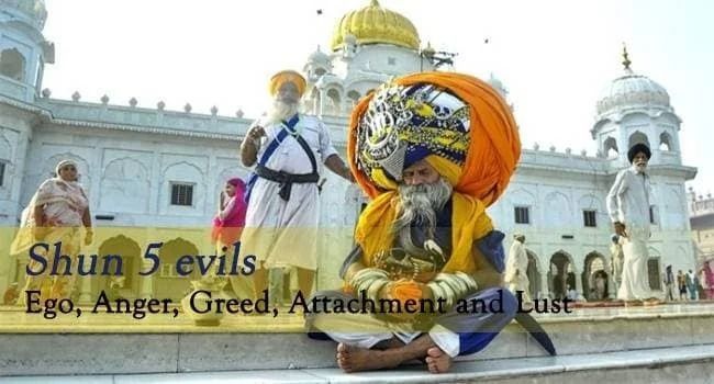 A man with a very large turban is sitting in front of a building.