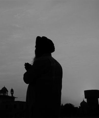 A silhouette of a man with a beard praying in front of a mosque.