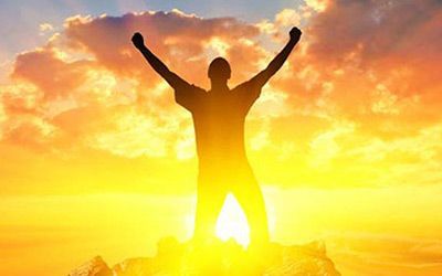 A silhouette of a man standing on top of a mountain with his arms in the air.