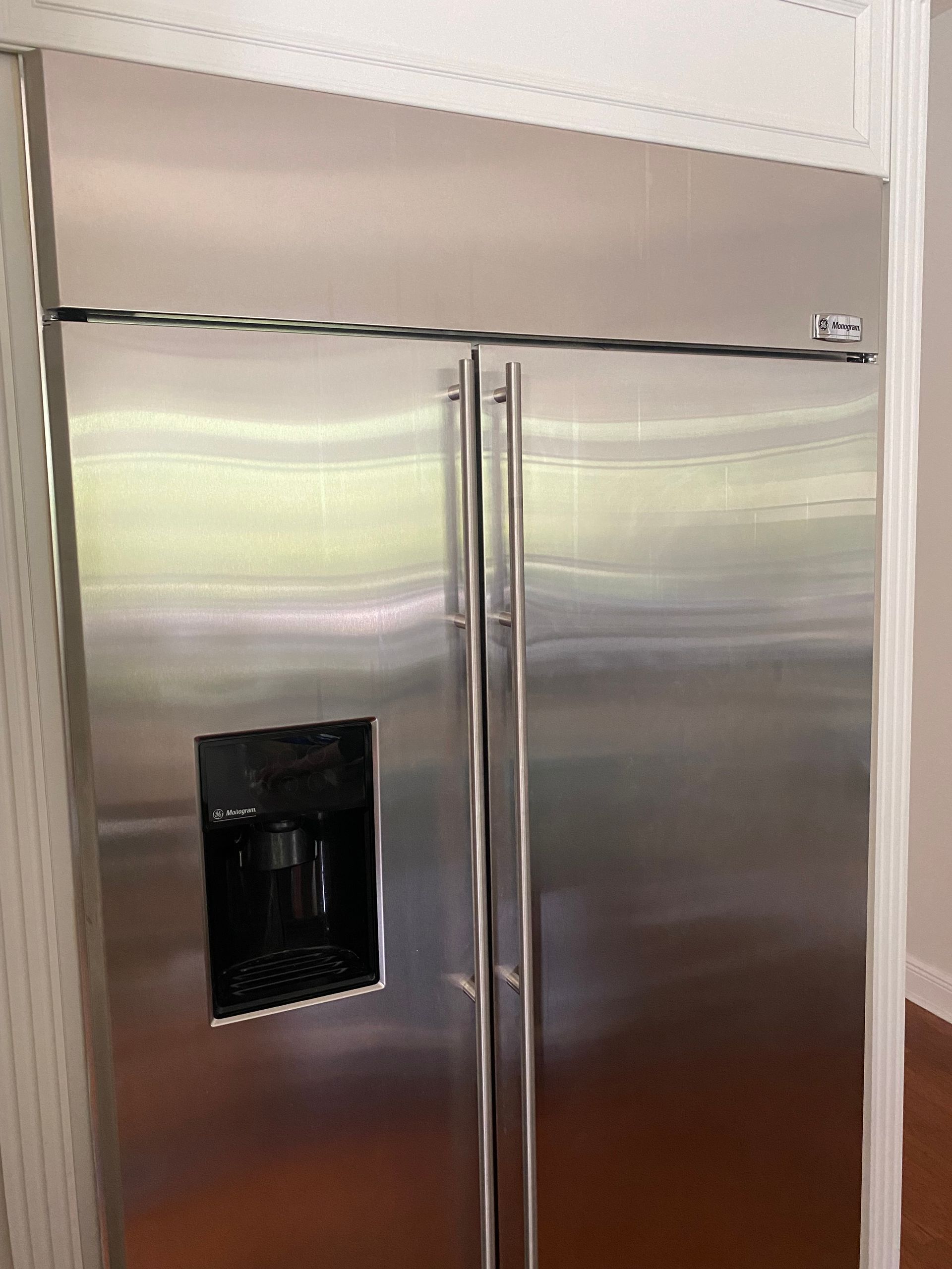 Stainless steel, side-by-side refrigerator built into a white framed space, with water dispenser.