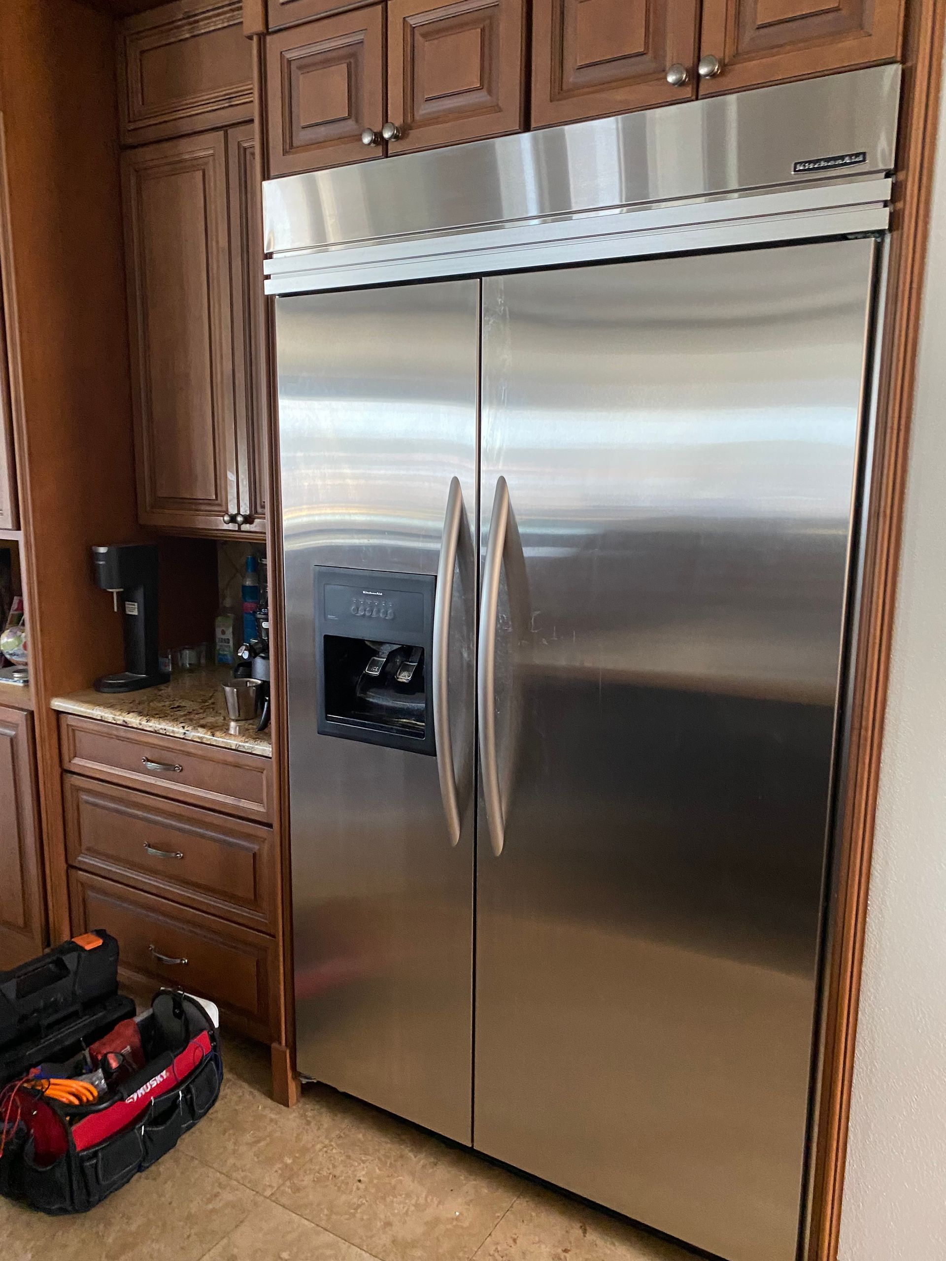 Stainless steel refrigerator in a kitchen with brown cabinets.