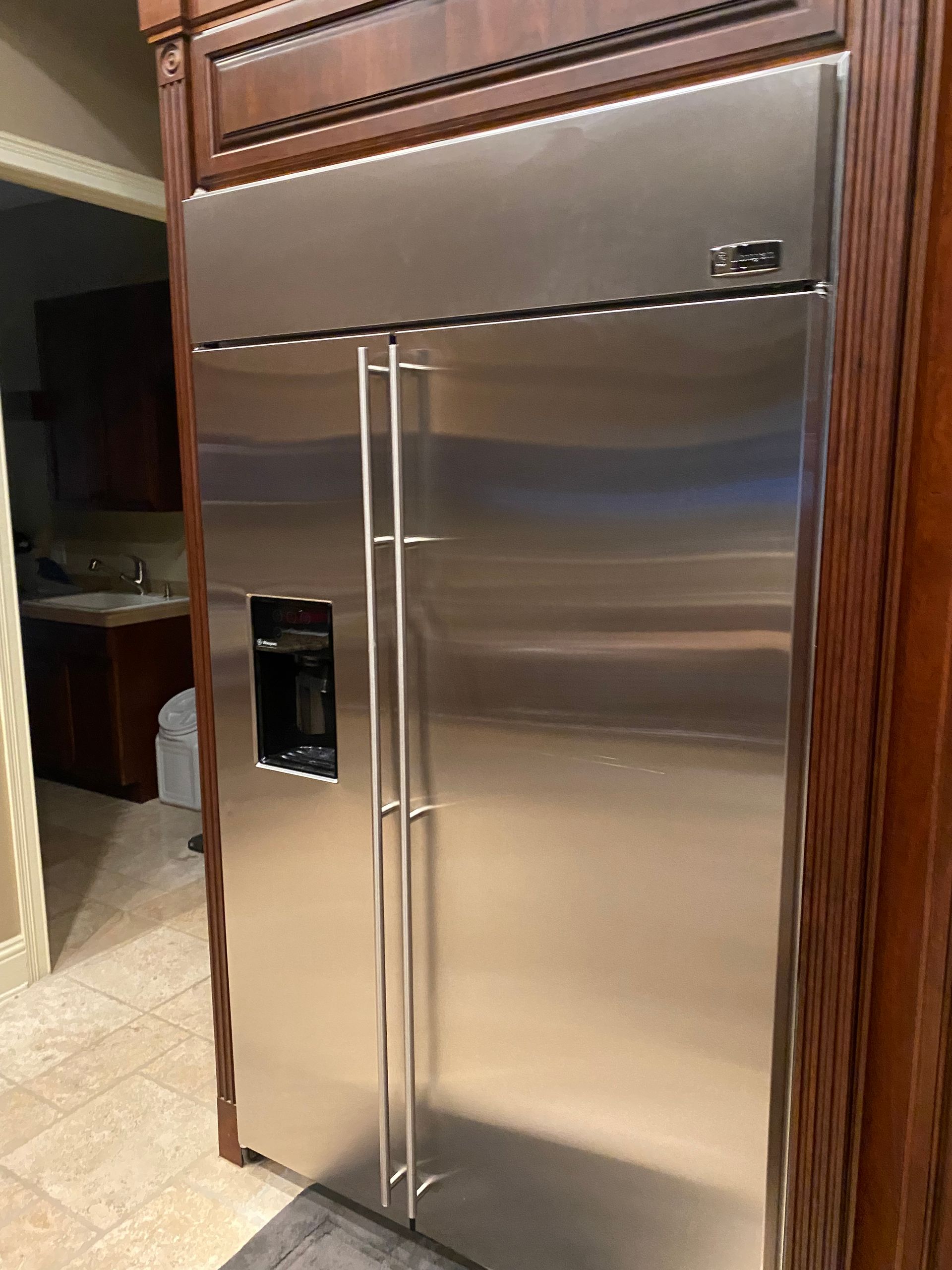 Stainless steel refrigerator with water dispenser, built-in between dark wood cabinets, in a kitchen.