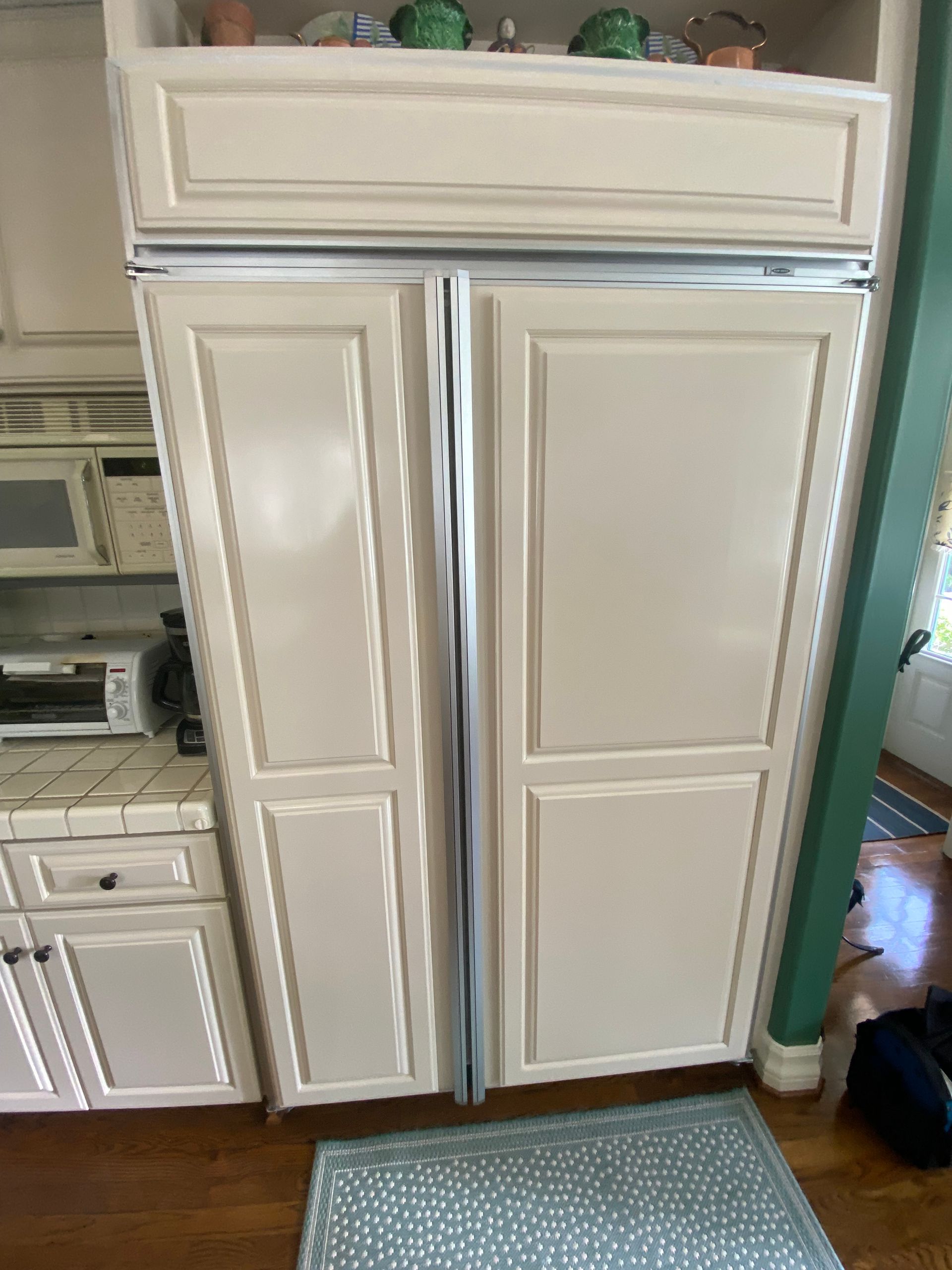 Cream-colored built-in refrigerator with two doors. It's in a kitchen next to cabinets and a counter.