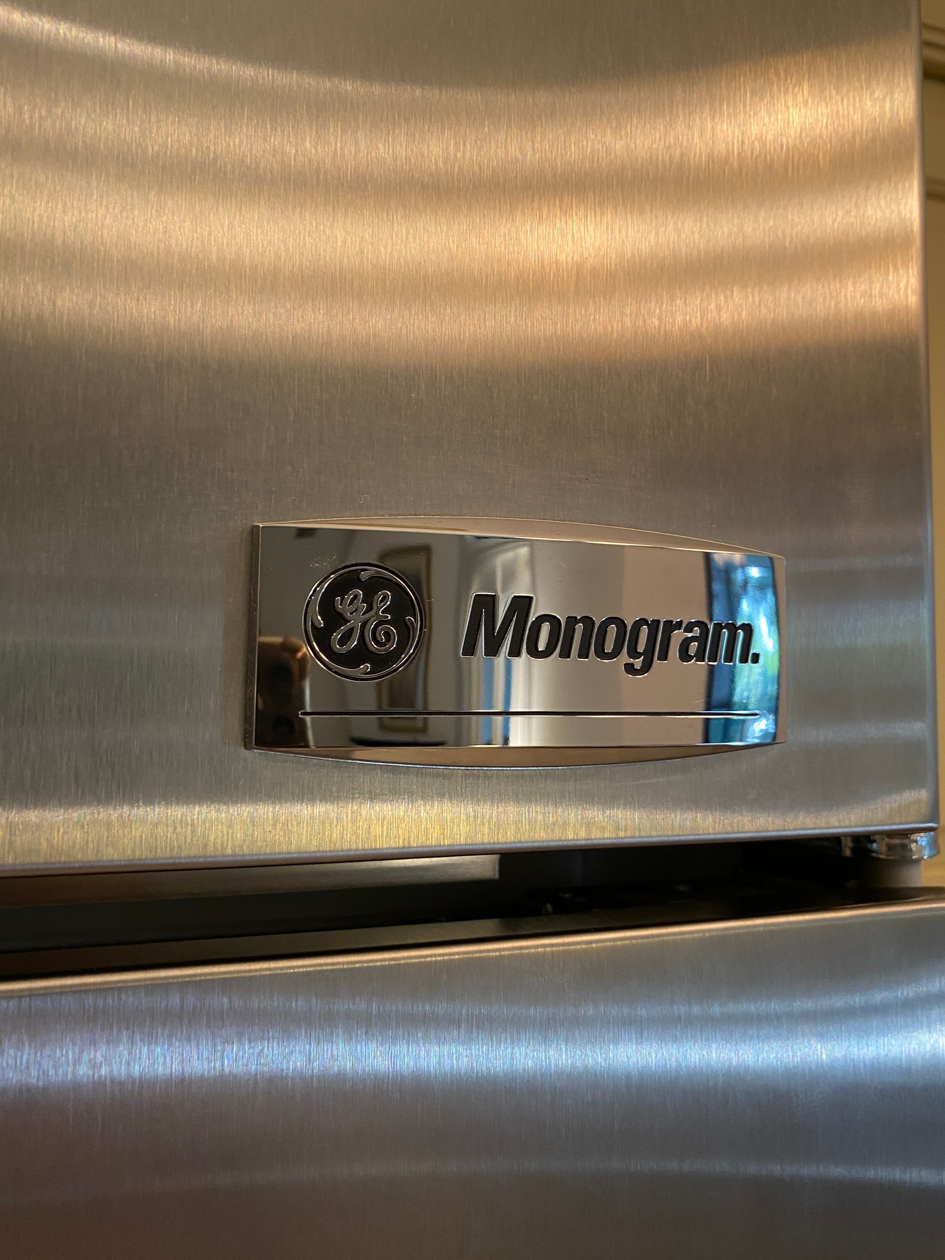 Stainless steel refrigerator door with GE Monogram logo.